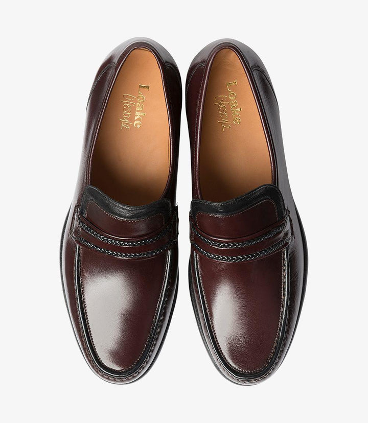 Both loafers are placed side by side from above, showing the moccasin’s classic shape and the subtle stitching details on the top. The burgundy leather’s finish and the rounded toe create an elegant look, with the wide fitting visible across the instep.