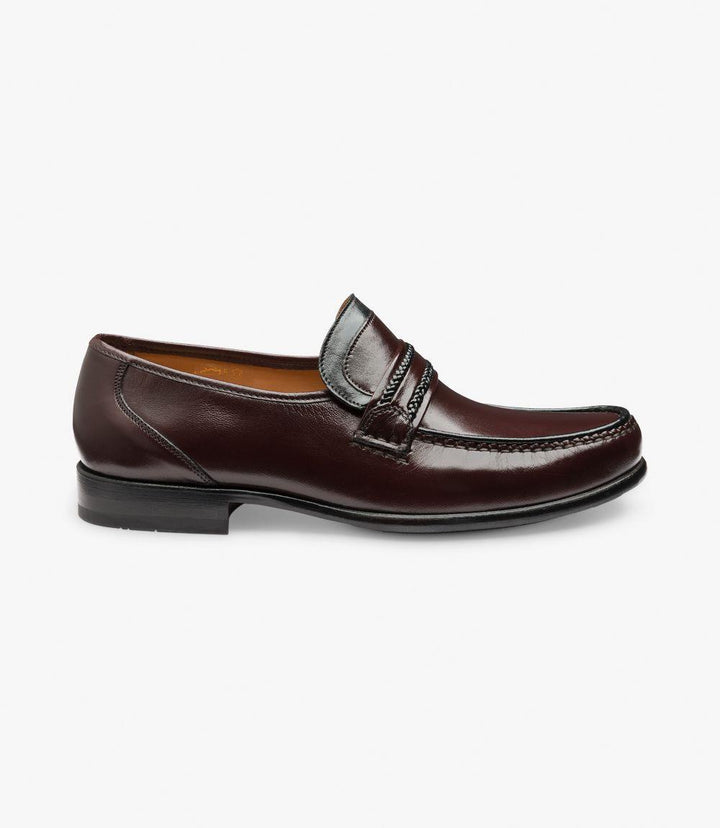 The Loake Rome Burgundy Loafer is shown from the side, highlighting its smooth, premium Nappa leather with a rich burgundy tone. The shoe’s moccasin construction and rounded toe shape are clear, as is the sturdy, flexible leather sole. Fine stitching along the edges adds a touch of craftsmanship.