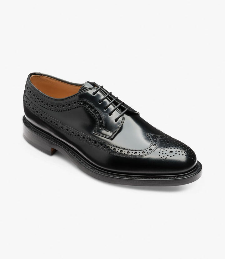 From an angled perspective, the shoe’s classic Derby lace-up construction is clearly visible, along with the full detailing of the brogue pattern extending around the toe cap and heel. The polished black leather gleams, highlighting the shoe’s high-quality craftsmanship and sleek silhouette.