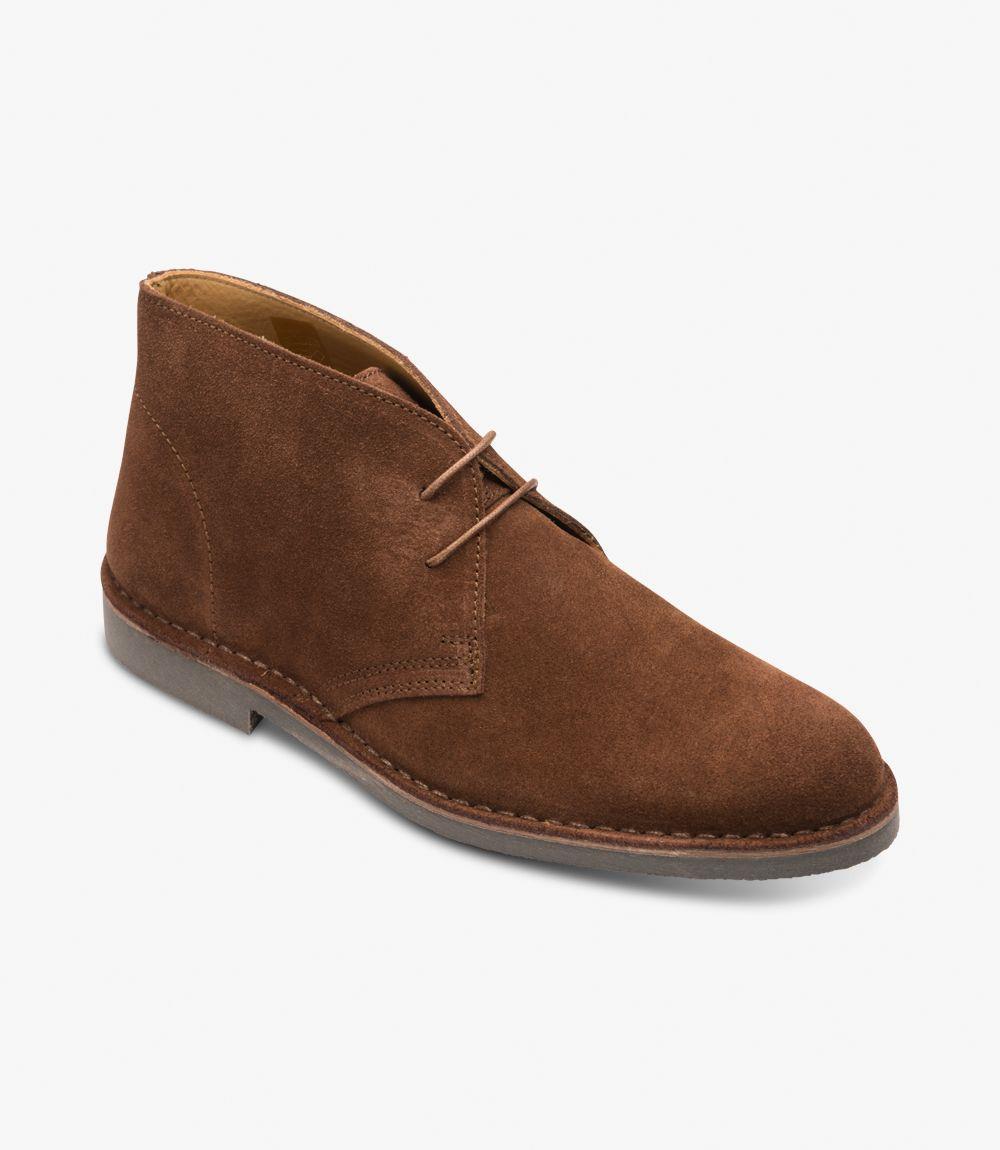 This angle view captures the Sahara Tan Chukka Boot from a slight diagonal perspective, offering a dynamic look at its stylish form. The boot's upper, crafted from premium suede, is beautifully complemented by the contrast of the stitched rubber sole. The three eyelets of the lacing system provide a glimpse of the soft leather lining within. The slightly elevated heel enhances the boot's silhouette, while the overall shape maintains a modern yet timeless appeal. 