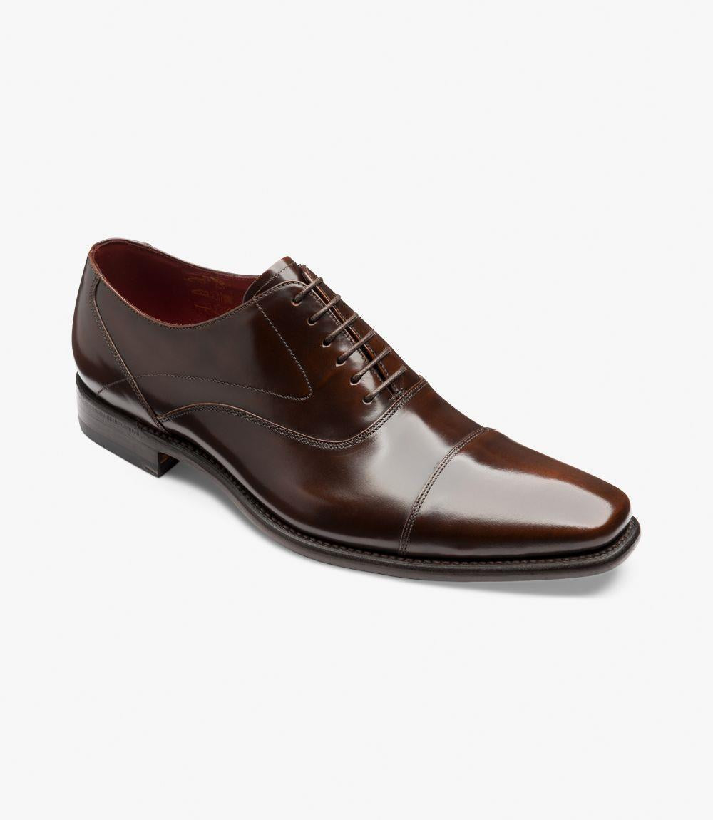 This angled view of the Loake Sharp Oxford captures the shoe's sophisticated lines and attention to detail. The polished dark brown leather gleams under the light, accentuating the fine grain and smooth texture. The classic toe cap is clearly defined, adding a touch of refinement. The angled perspective also highlights the contours of the shoe, including the curved collar and the elegant curve of the sole, creating a sense of movement and style.