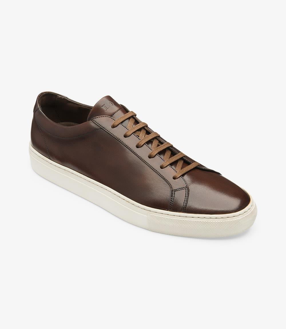 The angled view of the Loake Sprint Dark Brown Sneaker highlights the shoe's elegant profile and unique design elements. From this perspective, the hand-painted leather gleams with a luxurious finish, showcasing the artisanal quality of the craftsmanship. The cup rubber sole is clearly visible, providing a sturdy base that enhances both style and functionality. The bold toe shape and generous fit are evident, suggesting comfort without sacrificing sophistication. 