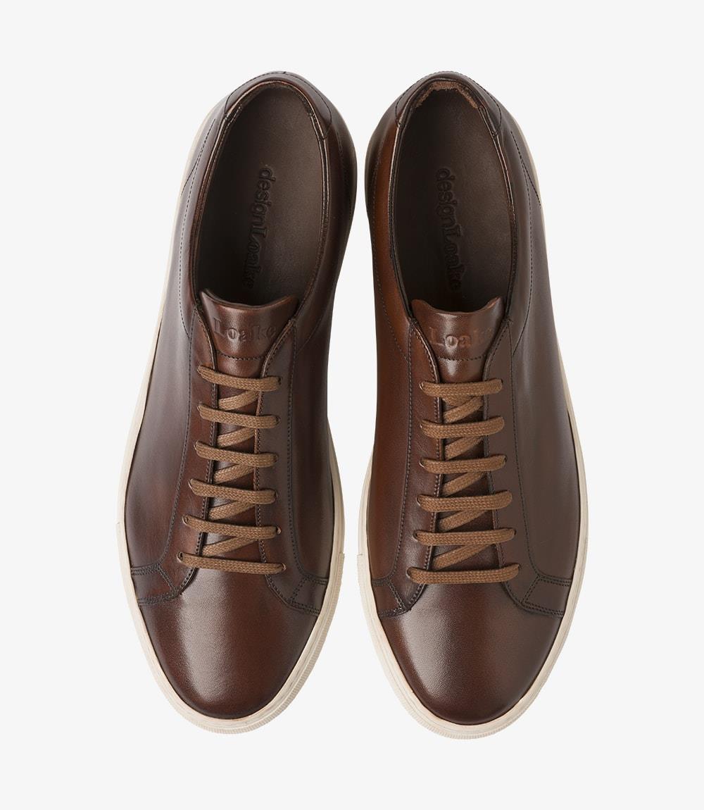 The top-down view of the Loake Sprint Dark Brown Sneaker reveals its classic loafer-inspired design. The sleek upper features minimalistic lines, while the round toe offers ample space for the toes, contributing to the overall comfort of the shoe. The hand-painted finish creates a rich visual texture, and the fully leather-lined interior is subtly visible, emphasizing the luxurious feel of the sneaker. The lacing system is neatly integrated into the design, adding to the overall streamlined appearance. 