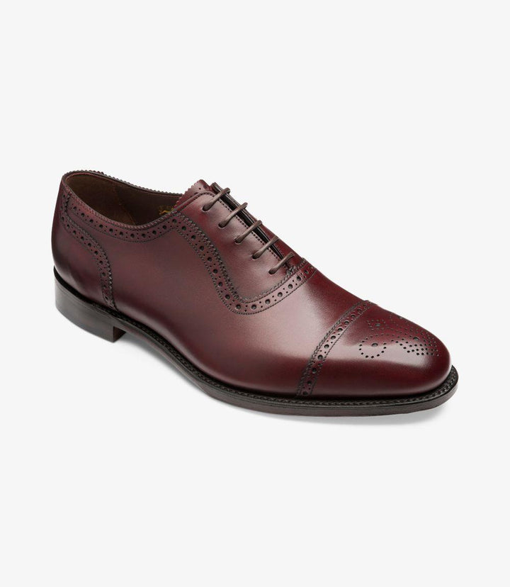 From an angled perspective, the shoe showcases the exquisite craftsmanship, with the intricate punched decorations accentuating the semi-brogue style. The slight curve of the shoe's profile leads the eye towards the slightly chisel-shaped toe, giving it a modern yet classic look. The interplay of light on the burnished leather further accentuates its quality and sophistication.