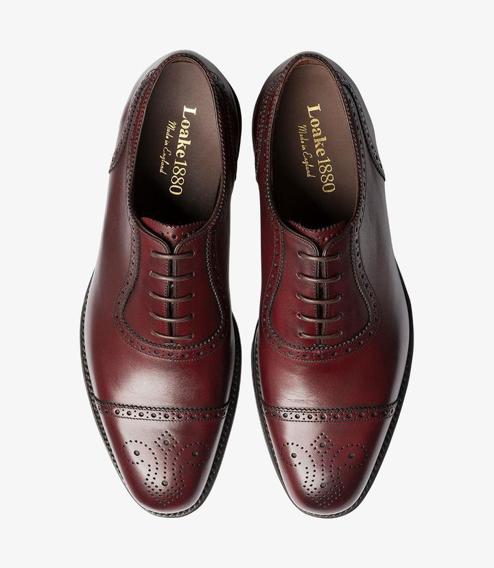 The top view reveals the classic Oxford design of the Loake Strand shoe, with the lace-up closure centered for a balanced aesthetic. The smooth burgundy leather surface is complemented by the elegant brogue detailing, while the structured upper maintains its shape. The refined lines and curves of the shoe create a sense of sophistication, making it a versatile addition to any wardrobe. The visible Goodyear welt at the edges underscores its durability and quality craftsmanship.