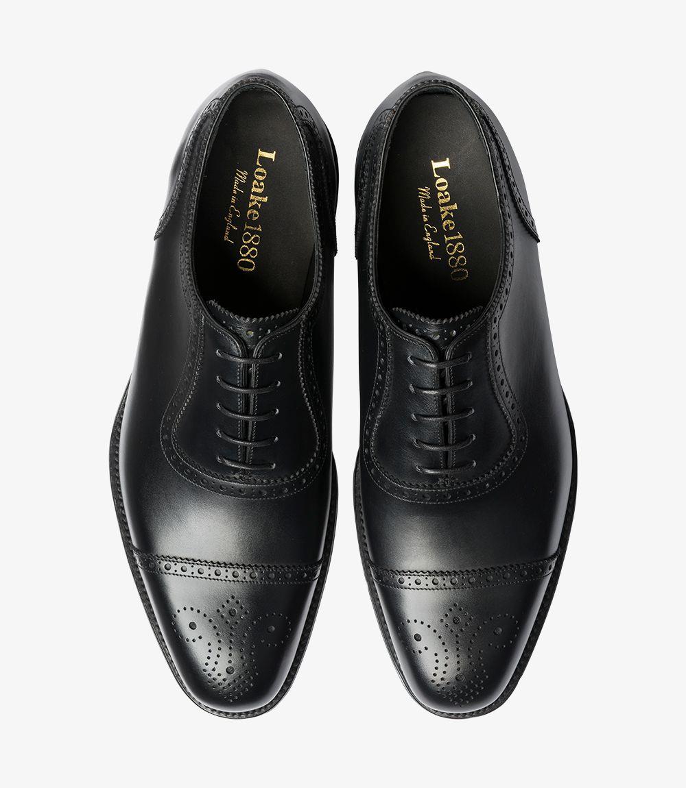 The top view of the Loake Strand Black Semi-Brogue shoe captures the elegant silhouette and classic Oxford design. The smooth burnished calf leather exhibits a rich, lustrous finish, while the intricate brogue detailing around the wing cap is prominently displayed. The lace-up closure is centered, showcasing the symmetrical lines that enhance its refined appearance. The slightly chisel-shaped toe can be seen, contributing to the shoe’s sophisticated profile.