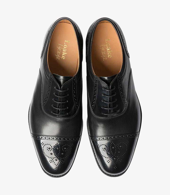 The top view of the Loake Woodstock Black Oxford Semi Brogue presents a symmetrical and elegant appearance. The smooth black leather upper is complemented by the neatly arranged lacing system, with five eyelets leading to the rounded toe. The semi brogue detailing is prominently displayed, with decorative perforations framing the shoe’s classic shape. This perspective emphasizes the shoe's polished finish and highlights the quality of materials used.